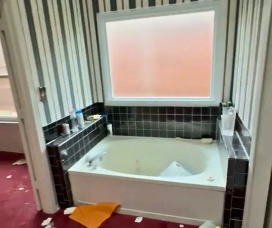 Before photo: dated jetted tub with dark tile surround and striped wallpaper