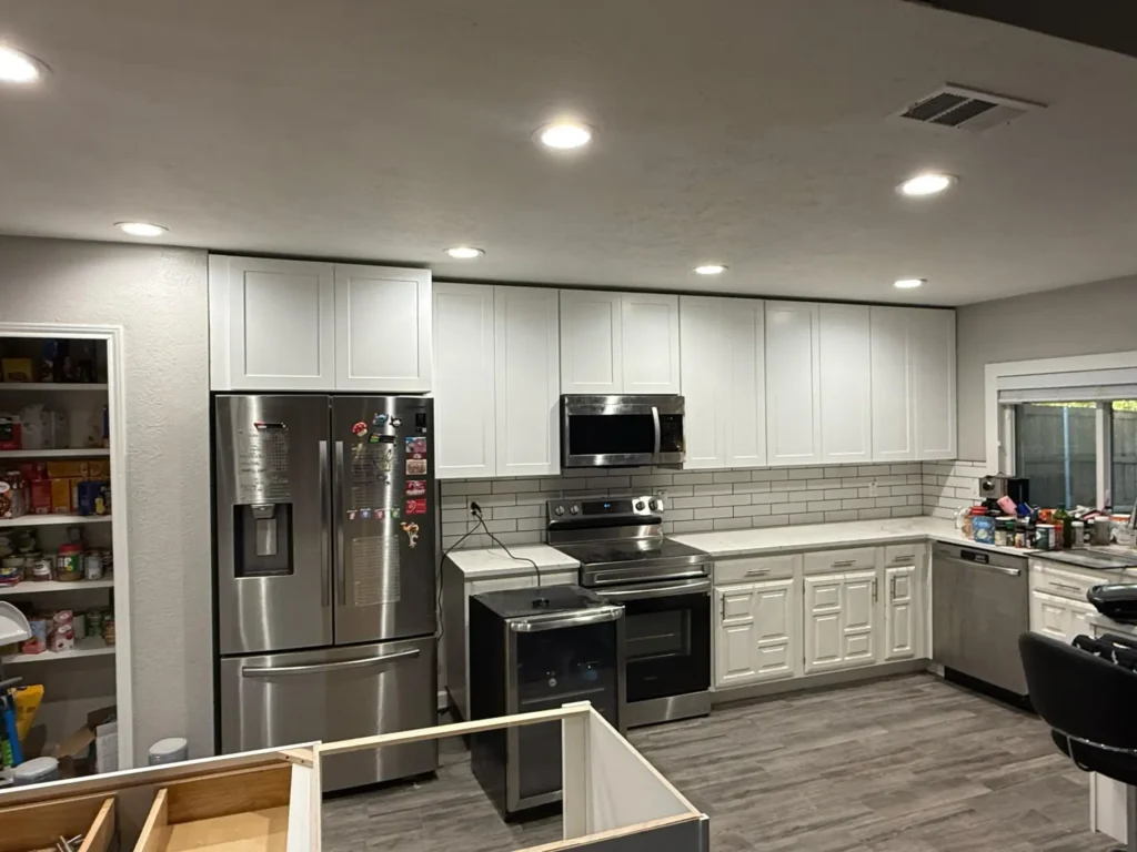This bright, modern kitchen features white shaker-style cabinetry, a white subway tile backsplash, and stainless steel appliances set against gray wood-look flooring.