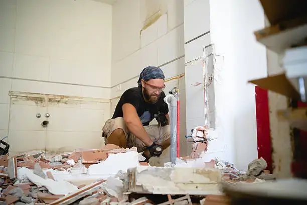 Worker removing tiles and pipes during a messy bathroom remodel.