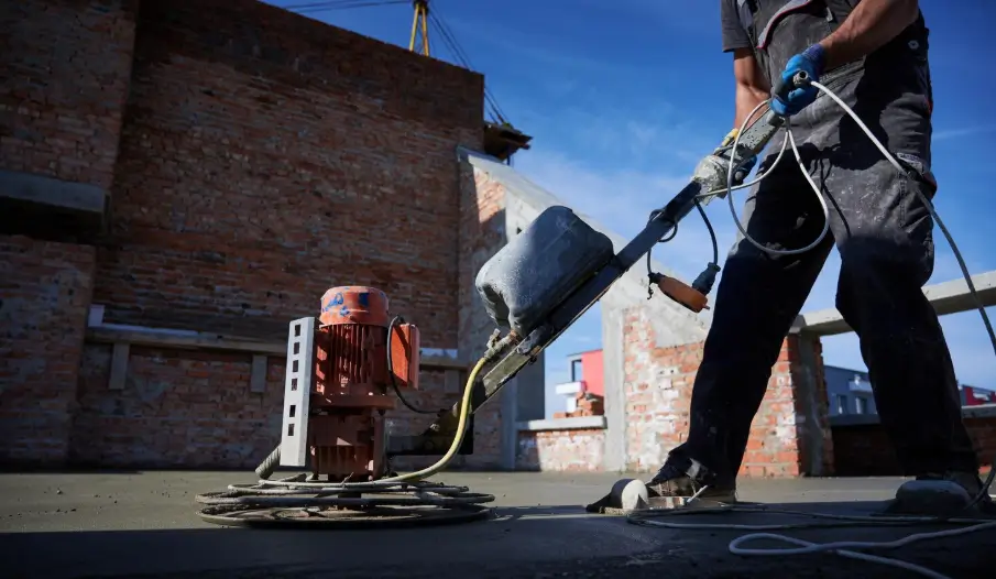 A worker operates a power trowel to smooth a fresh surface, preparing the substrate for the eventual application of a protective concrete sealer.