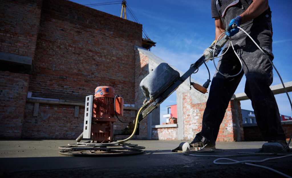 Cropped picture of man laborer in work overalls using power trowel machine while concrete cleaning the floor in new building. 