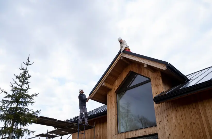 Two construction workers collaborate from a rooftop and scaffolding to conduct a final roof inspection on a newly finished modern wooden home.