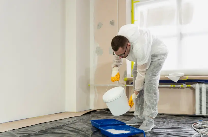 A professional painter in protective gear carefully pours paint into a tray, preparing the essential materials for a high-quality interior painting project.