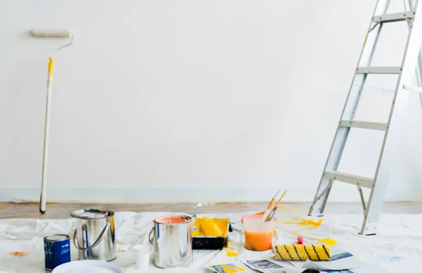 Open paint cans, rollers, and a ladder are neatly arranged in a bright room during the early stages of a professional interior painting renovation.