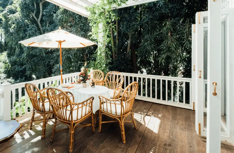 An elegant wooden deck features a dining set with wicker chairs and a white umbrella, all tucked beneath lush greenery and integrated patio covers for a comfortable outdoor experience.