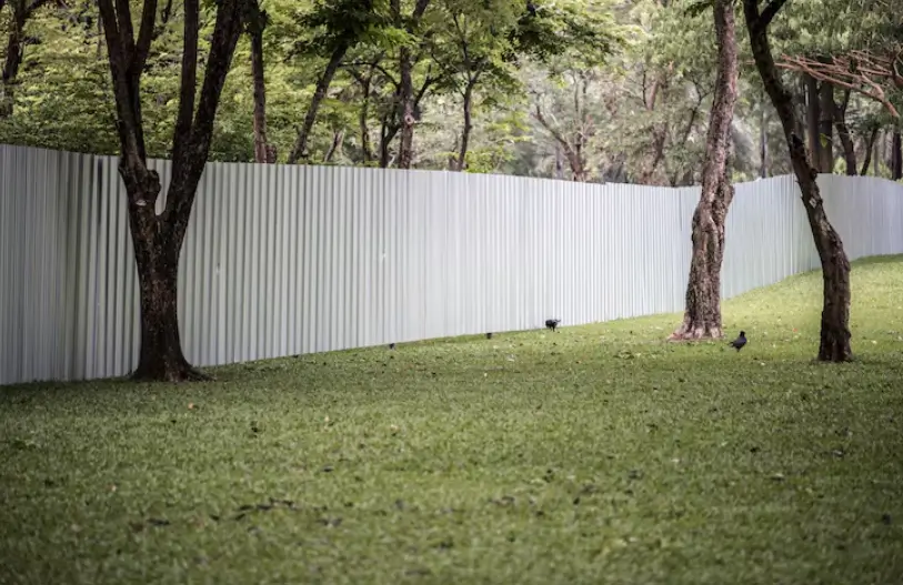 A long, silver corrugated metal barrier snakes through a grassy wooded area, providing a secure boundary as a result of professional fence installation.