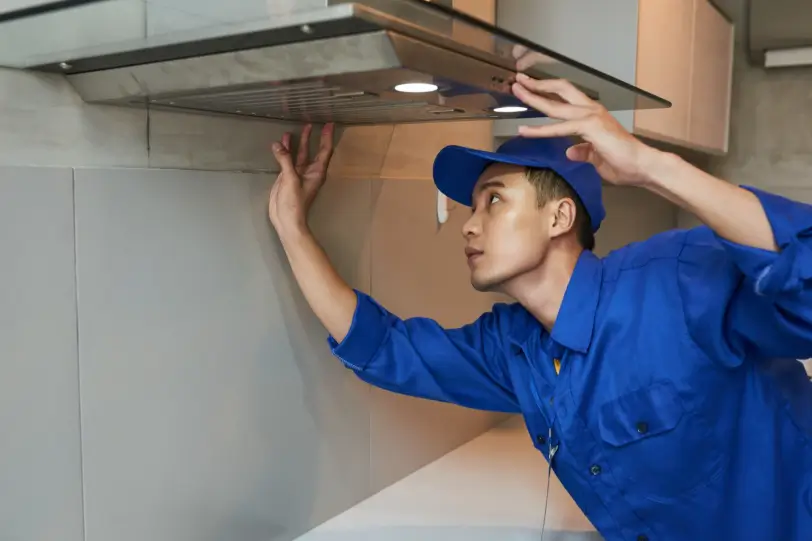 A professional technician in a blue uniform inspects a kitchen ventilation system, which is a vital part of the internal structure that often requires professional chimney repair and maintenance.