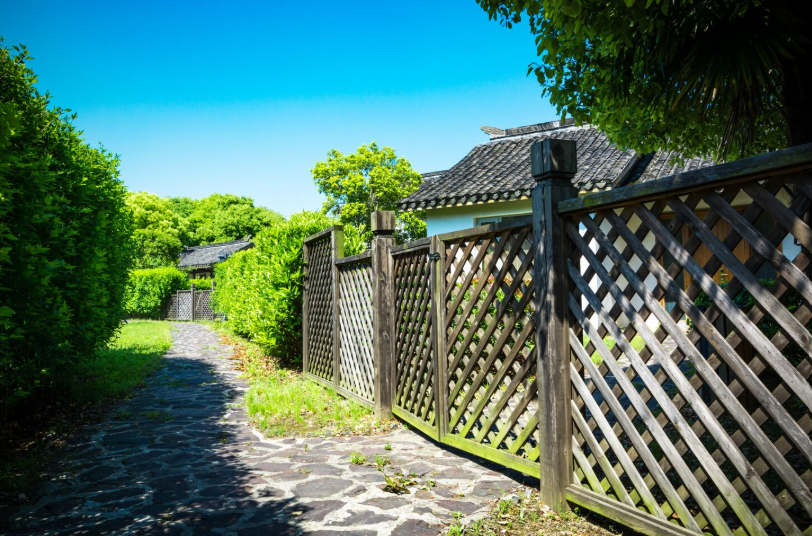 A classic wooden lattice structure borders a stone pathway and lush green hedges, providing a decorative and traditional fence style for the garden.