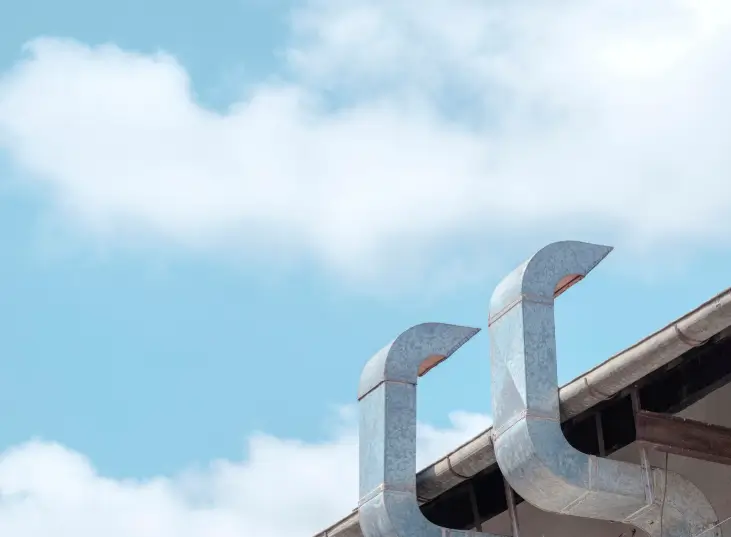 Modern stainless steel exhaust pipes and outdoor ventilation ducts extend toward the sky, illustrating the essential structural components that benefit from regular professional chimney cleaning.