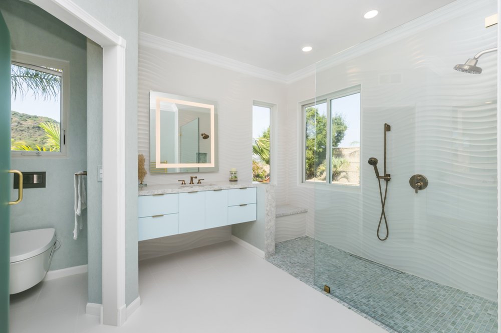 Bright white bathroom remodel with walk-in glass shower and floating vanity by Akraba Remodeling