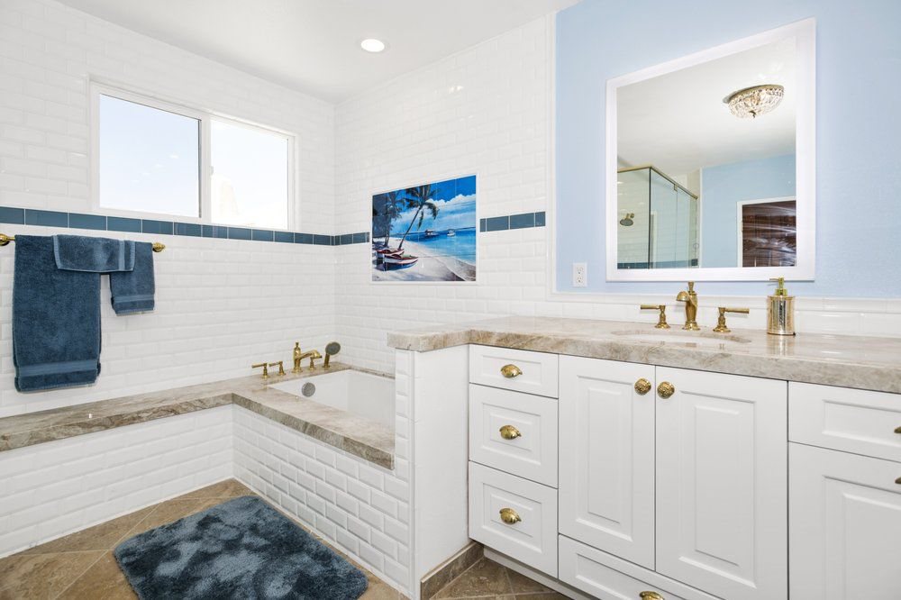 Remodeled bathroom with white cabinets, stone counters and a backlit mirror by Akraba Remodeling