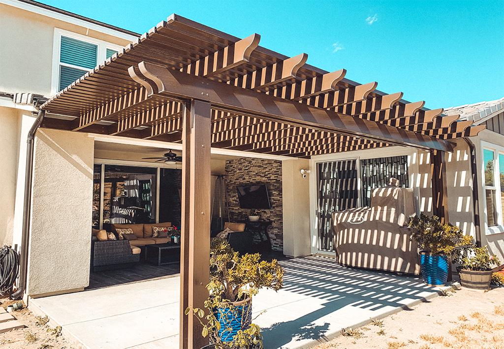 Brown pergola with open rafters shading a back patio and outdoor seating area