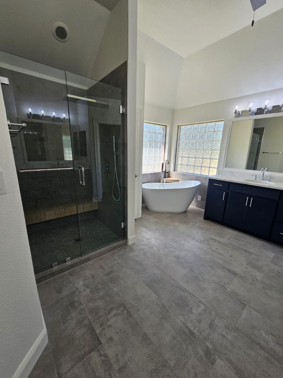 Primary bathroom remodel with a glass walk-in shower, freestanding tub and navy vanity by Akraba Remodeling