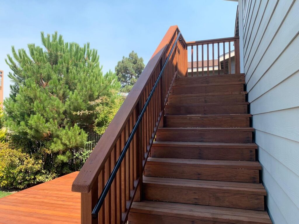 Stained wood deck stairs with a black handrail by Akraba Construction LLC, serving Coppell, TX