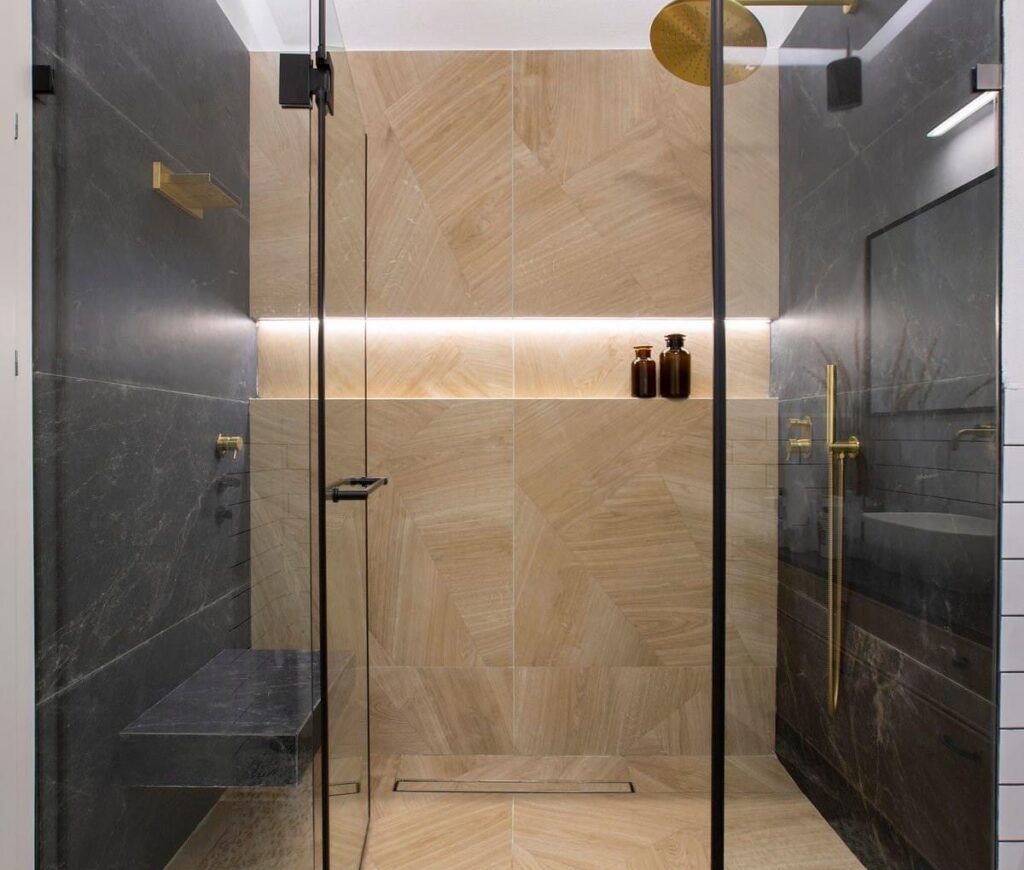 Walk in shower with glass doors, gold fixtures and a lit niche by Akraba Construction LLC, serving Carrollton, TX