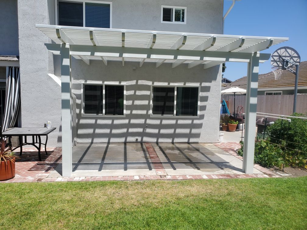 White pergola shading a backyard concrete patio along the back of the house